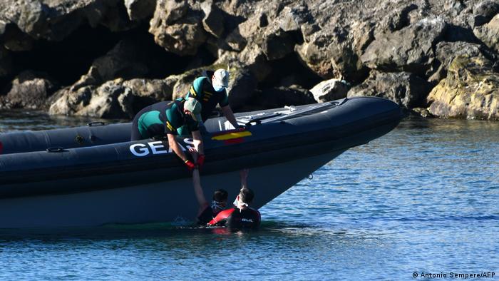 Spanish Civil Guards pull migrants into inflatable boat.