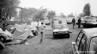 Autos auf einer Wiese mit aufgeschlagenen Zelten dazwischen