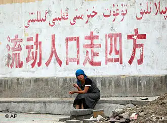 A Uighur woman sits under an official slogan says in Chinese Population flow spread in all directions at Uighur sector in Urumqi, western China's Xinjiang province, Tuesday, July 14, 2009. The capital of China's western Xinjiang region was tense amid tight security Tuesday, a day after police fatally shot two Uighur men and wounded a third, more than a week after deadly ethnic rioting. (AP Photo/Eugene Hoshiko)