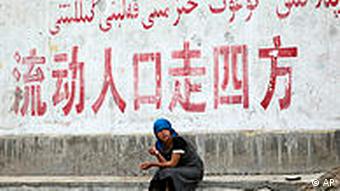 A woman sits under a sign reading Population flow spread in all directions - Uighurs now make up less than half of Xinjiang's population