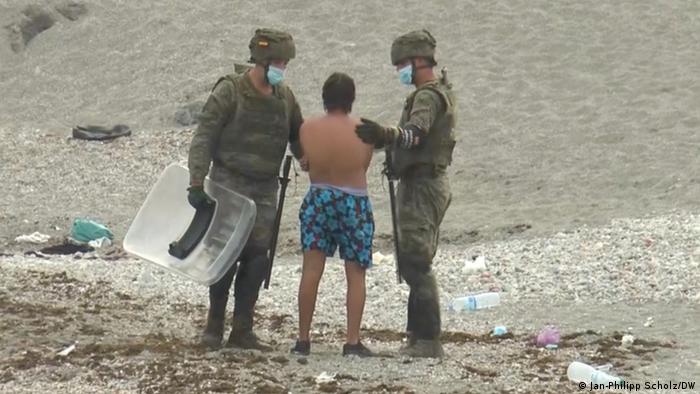 Two Spanish soldiers talk to a young man who just swam onto a Ceuta beach