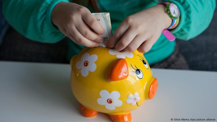 A kid putting money in a piggy bank 