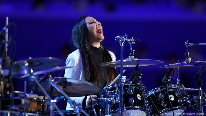 Sheila E. smiling with head held back and sitting behind drums. 