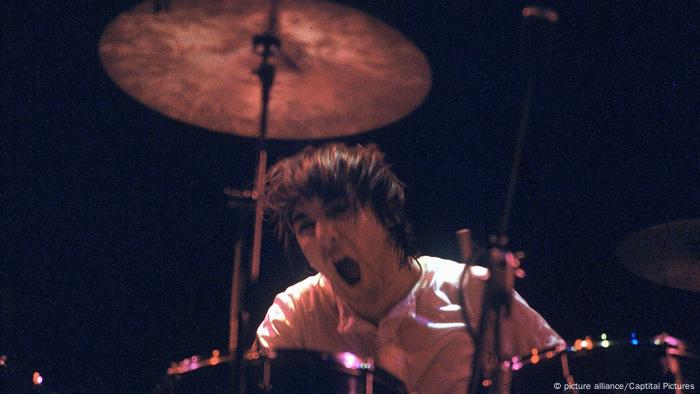 Keith Moon playing on the drums with his mouth wide open.