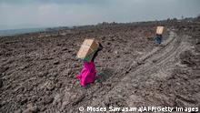 25.05.2021
TOPSHOT - Residents carry goods on their backs while they cross a lava covered field in Buhene, north of Goma on May 25, 2021. - The city of Goma, in the east of the Democratic Republic of Congo (DRC), was in anguish on Tuesday of a new eruption of the Nyiragongo volcano towering over the city, where long cracks fractured the ground shaken by violent earthquakes repeat. (Photo by Moses Sawasawa / AFP) (Photo by MOSES SAWASAWA/AFP via Getty Images)