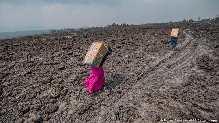 People carry goods on their backs while crossing a field covered in lava near Goma