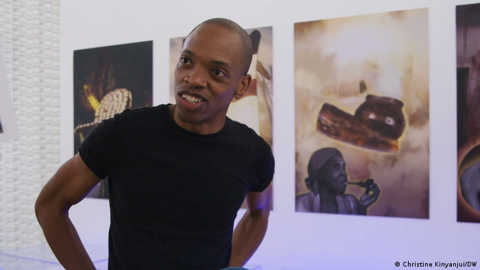 The artist Jim Chuchu with pictures on the wall in the background.