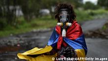 TOPSHOT - A demonstrator wrapped in a Colombian flag walks along the Panamerican highway, which is blocked to protest against the government of President Ivan Duque, between Buga and Cali, in Valle del Cauca department, Colombia, on May 26, 2021. - Officially, 43 people have died in clashes since protests started, initially against a proposed tax reform that has since been withdrawn. Demonstrations have continued in the face of a violent police crackdown that has drawn international condemnation. (Photo by LUIS ROBAYO / AFP) (Photo by LUIS ROBAYO/AFP via Getty Images)