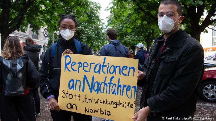 Demonstranten in Berlin tragen ein Pappschild mit der Aufschrift Reparationen an Nachfahren statt 'Entwicklungshilfe' an Namibia