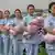 Fila de estudantes de enfermagem chinesas, vestidas com uniformes azuis-claros. Cada uma carrega um boneco-bebê envolto numa manta cor de rosa, durante cerimônia de formatura em maio de 2021 em Jinan, na província de Shandong.