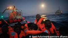 Migranten und Flüchtlinge verschiedener afrikanischer Nationalitäten reagieren in einem überfüllten Holzboot im Mittelmeer vor der Küste von Libyen, als sich ihnen Hilfsarbeiter der spanischen Hilfsorganisation «Open Arms» nähern. +++ dpa-Bildfunk +++