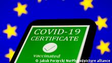 'COVID-19 certificate' sign displayed on a phone screen and European Union flag in the background are seen in this illustration photo taken in Krakow on April 29, 2021. (Photo Illustration by Jakub Porzycki/NurPhoto)