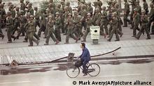 A Beijing bicyclist rides past a company of Chinese foot soldiers marching east down Changan Blvd. away from Tiananmen Square, Wednesday, June 7, 1989, Beijing, China. The troops were making a sweep after a convoy of several hundred trucks moved up the street firing indiscriminately in the air and into the foreign diplomatic compound from which this photo was made. (AP Photo/Mark Avery)