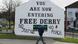 A young man walks past the notorious "You are now entering Free Derry" sign in the flashpoint border city of Londonderry in Northern Ireland. Archive image from 2019. A young man walks past the notorious "You are now entering Free Derry" sign in the flashpoint border city of Londonderry in Northern Ireland. Archive image from 2019.