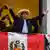 Perus gewählter Präsident Pedro Castillo breitet die Arme aus auf einem mit peruanischer Flagge geschmückten Balkon 