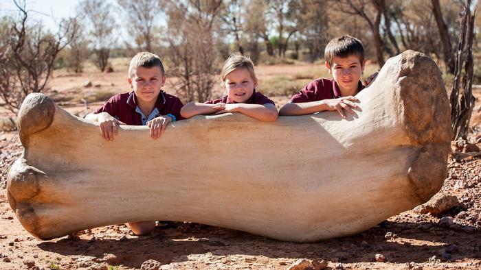 Los estudiantes posan para fotos con una réplica del fémur de Australotitan cooperensis en Eromanga, Queensland, Australia