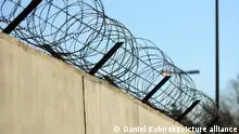 Symbolbild Freiheit / Unfreiheit, Gefangenschaft, Grenzen. Eine mit Stacheldraht bewehrte Betonmauer.