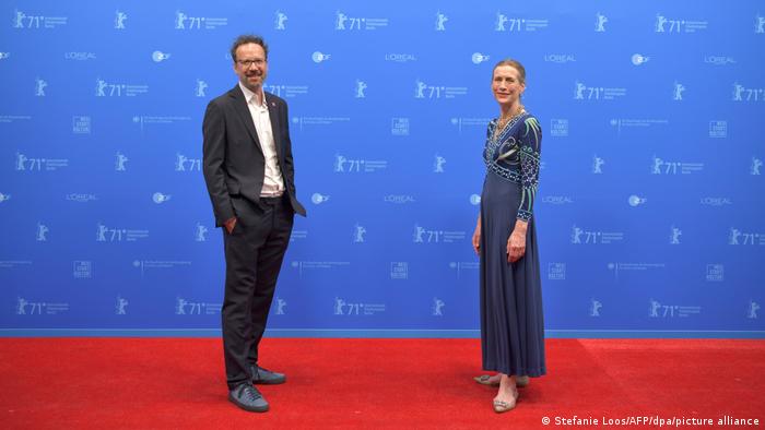 Carlo Chatrian im dunklen Anzug und Mariette Rissenbeek im blauen langen Kleid stehen - mit Abstand zueinander - auf dem roten Teppich der Berlinale und gucken in die Kameras.
