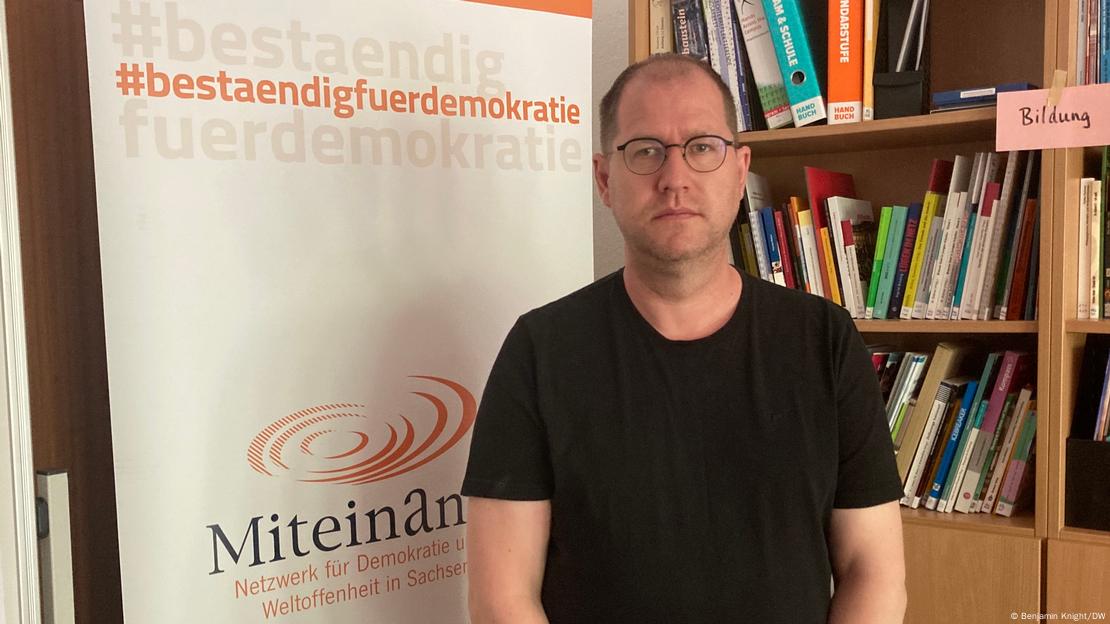 David Begrich steht vor einem Plakat des Vereins Miteinander in Magdeburg