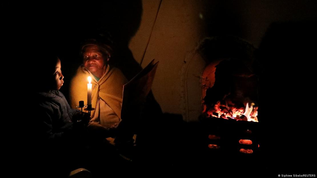 Una mujer mayor y su bisnieta, a la luz de una vela, mientras se calientan frente a una chimenea en Soweto, Sudáfrica.