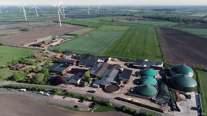 Luftaufnahme: Wind- und Solarparks von Sprakebüll (Norddeutschland) im Hintergrund. Solarpanelen auf dem Dächern vom Hof und eine Große Biogasanlage mit den grünen Dächern 
