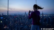 A woman holding a mobile phone stands before the Manhattan skyline prior to a partial solar eclipse, at the Edge viewing deck, in New York on June 10, 2021. - Northeast states in the US saw a rare eclipsed sunrise, while in other parts of the Northern Hemisphere, this annular eclipse will be seen as a visible thin outer ring of the sun's disk that is not completely covered by the smaller dark disk of the moon, a so-called ring of fire. (Photo by Ed JONES / AFP)