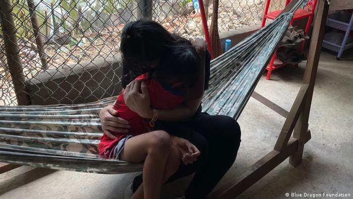 A woman hugs a child, their faces are covered 