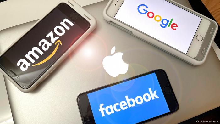 Smartphones liegen auf einem Laptop von Apple und zeigen die Logos von Amazon, Facebook und Google