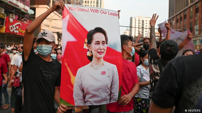 Myanmar demonstrators holding a banner with the figure of Suu Kyi and the slogan we stand with our leader.