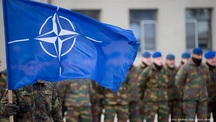 NATO flag bearer and troops in the background