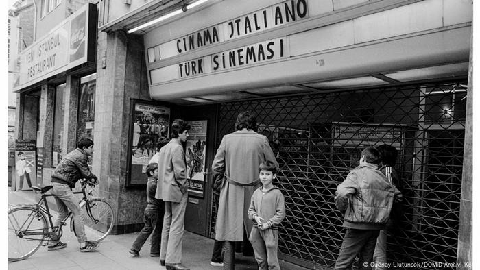 Schwarz-weiß Foto eines Kinos von außen, davor stehen ein paar Menschen. Über dem Eingang steht Cinama Italiano. Schwarz-weiß Foto eines Kinos von außen, davor stehen ein paar Menschen. Über dem Eingang steht Cinama Italiano.