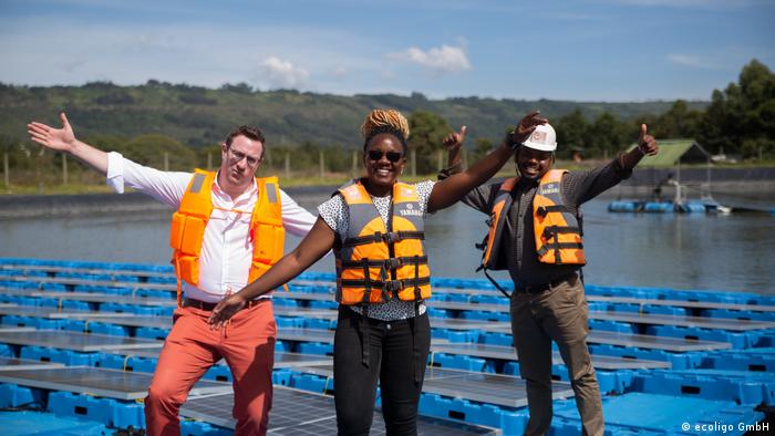 Mitarbeiter mit Schwimmwesten stehen lachend auf Schwimmern einer Solaranlage in Kenia. 