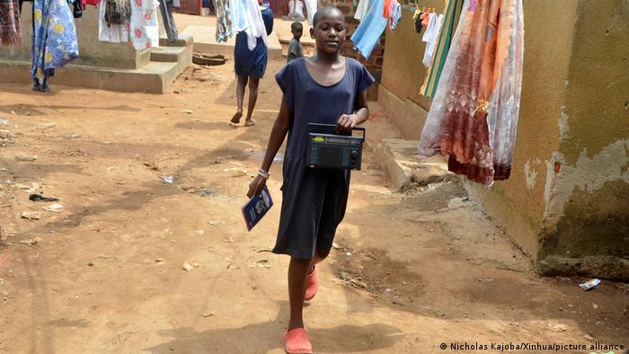 A student in Kampala is seen walking to school with a radio in her hand