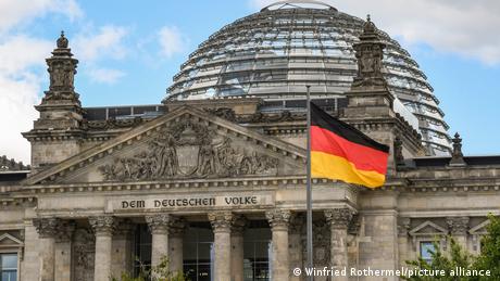 A German flag is raised in front of the German parliament in Berlin