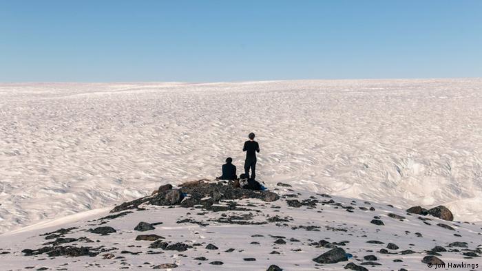 Two people looking out over Greenland's icy landscape from a hill
