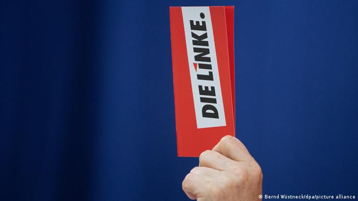A hand holds up a sign with the logo of the Left Party (Die Linke)