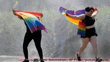 A women with a rainbow flag cools off in a sprinkler ahead of the Equality Parade, the largest LGBT pride parade in Central and Eastern Europe, in Warsaw, Poland, Saturday, June 19, 2021.(AP Photo/Czarek Sokolowski)