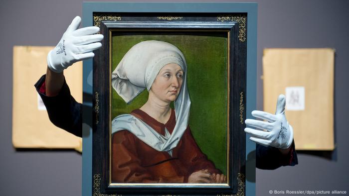 Ein Gemälde, das eine mittelalterlich gekleidete Frau zeigt, wird von zwei Händen in weißen Handschuhen umgeben. Ein Gemälde, das eine mittelalterlich gekleidete Frau zeigt, wird von zwei Händen in weißen Handschuhen umgeben.