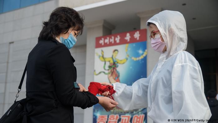 Mulher de veste protetora tira temperatura em pulso de mulher de máscara sanitária