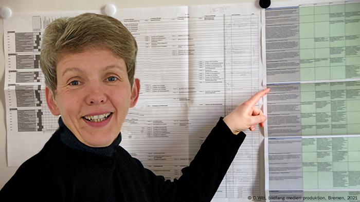 Irmhild Rogalla pointing at an item on a list pinned to a board
