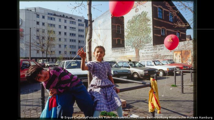 Two children with balloons in front of a parking lot. 