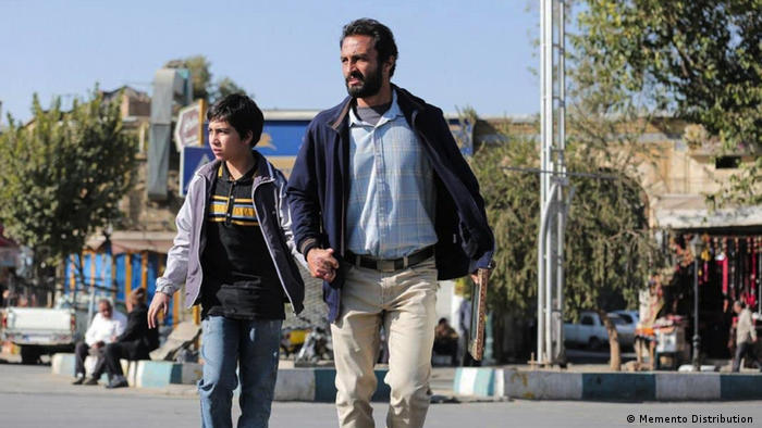 Film still 'A Hero': a man holds a child's hand as they walk in an urban setting.