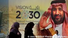 People walk past a banner showing Saudi Crown Prince Mohammed bin Salman, outside a mall in Jiddah, Saudi Arabia, Friday, Dec. 6, 2019. Arabic reads, vision of 2030. (AP Photo/Amr Nabil)