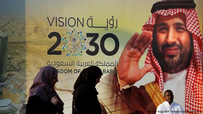 People walk past a banner showing Saudi Crown Prince Mohammed bin Salman, outside a mall in Jiddah, Saudi Arabia.