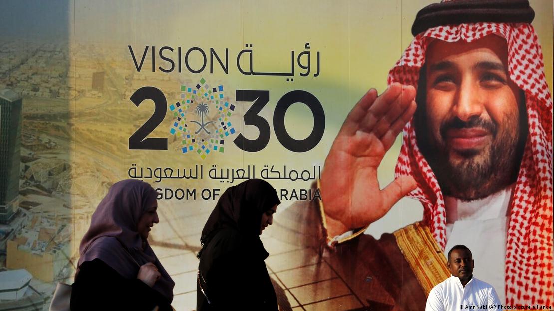 People walk past a banner showing Saudi Crown Prince Mohammed bin Salman, outside a mall in Jiddah, Saudi Arabia.