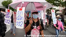 A protester holds a pink umbrella with signs hanging from it and writing in Thai