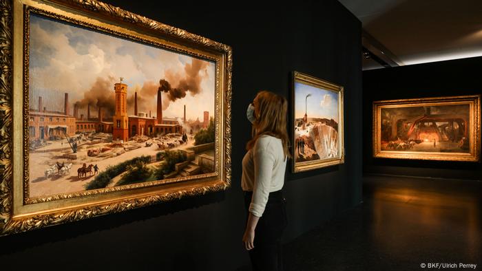 Eine Frau mit Mund-Nasenschutz betrachtet ein Gemälde mit rauchenden Schloten in der Ausstellung Moderne Zeiten, Bucerius Kunst Forum Hamburg Eine Frau mit Mund-Nasenschutz betrachtet ein Gemälde mit rauchenden Schloten in der Ausstellung Moderne Zeiten, Bucerius Kunst Forum Hamburg