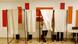 Four voting booths with two people inside - one of them, a woman, is emerging. Four voting booths with two people inside - one of them, a woman, is emerging.