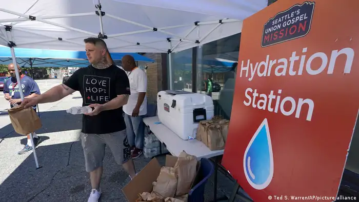 Carlos Ramos hands out bottles of water and sack lunches as he works at a hydration station in front of the Union Gospel Mission in Seattle