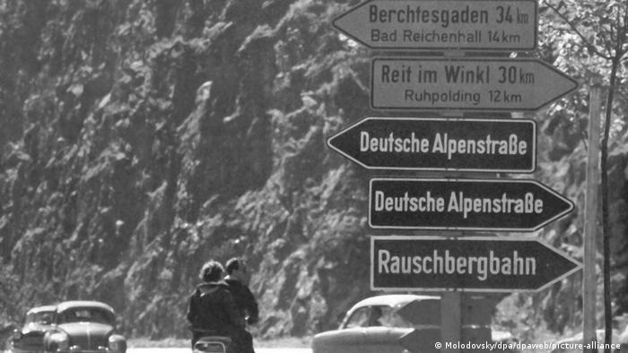 Foto antiga mostra placas de orientação para motoristas sobre a rota dos Alpes